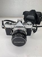 Front view of Olympus OM-1 with lens cap on, leather case in background