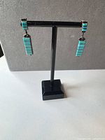 Front view of both turquoise inlay sterling silver drop earrings on stand