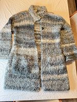 Full front view of long fuzzy gray and cream cardigan coat showing overall design, collar, button and pockets