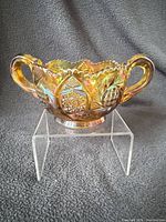 Front view of amber carnival glass sugar bowl showing twin handles, hobstar pattern and iridescent finish