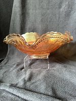 Side profile of ruffled marigold Dugan punch bowl on acrylic stand