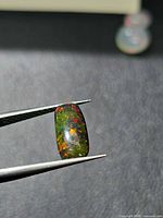 Opal held in tweezers showing play-of-colour