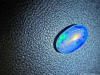 Opal cabochon on textured black background showing blue body and multicolour flash