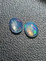 Pair of oval crystal jelly opals showing play-of-color on textured background