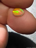 Close-up of oval golden crystal opal showing green and yellow play-of-color