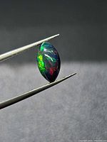 Side view of marquise cabochon Ethiopian black opal held in tweezers