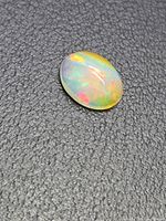 Opal cabochon top view on textured background showing body colour and play of colour