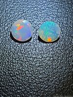Pair of round faceted opals showing play-of-color face-up on textured background