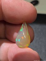 Pear-shape opal showing multicolor play-of-color held between fingers
