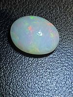 Top view of oval crystal opal on black background showing multicolored play of color