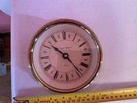 Front view of brass ship-style quartz wall clock with ruler for scale