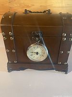 Front view showing wooden chest, clock insert, metal studs, feet