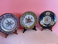 Front view of three 10-inch tin coronation plates on stands