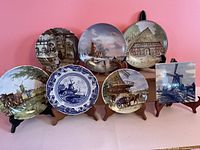 Seven decorative Dutch-themed plates on stands against pink background