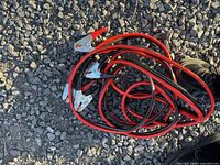 Coiled red and black jumper cables with metal clamps on gravel surface