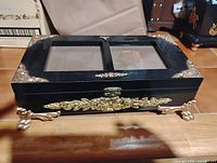 Top view of black wooden box showing dual glass panels and gold-tone decorative accents