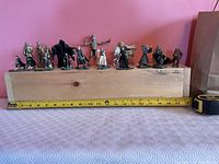 Front view of all 14 figurines lined on wooden block showing scale against tape measure