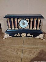 Front view of black and gold mantel clock showing columns, dial and decorative feet