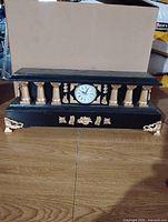 Front view of black and gold handmade mantel clock showing columns, dial, decorative feet