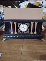 Front view of black mantel clock with columns, dial and decorative feet