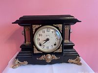 front view of black wooden mantel clock with white dial and ornate brass mounts