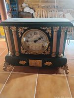 Front view of black and gold mantel clock with ornate columns and feet