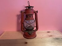 Front view of red BAT No. 158 hurricane lantern on wooden surface, showing glass globe, frame and fuel cap