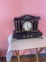 Front view of black metal mantel clock showing dial, columns and gold accents