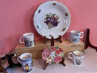 Group photo showing large fruit motif plate, small floral plate, four scenic mugs