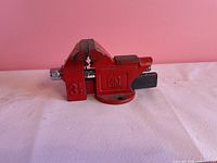 Side view of red Home Hardware 3.5 in swivel bench vise on white surface