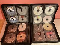 Open view of two black zippered binders showing multiple discs including Elvis, Train, The Daily Show, MIA