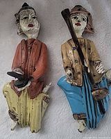 Front view of both carved wooden figurines showing colors, instruments and size