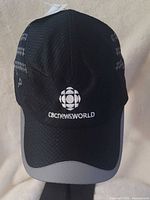 Front view of black CBC NewsWorld cap showing embroidered logo and brim detail