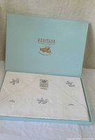 Open box displaying folded white embroidered sheets with tag