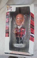 Front of unopened tartan-pattern box with clear window showing Don Cherry bobblehead on base labeled CHERRY