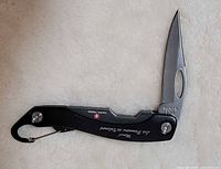 Knife open showing blade, thumb hole, handle branding, and carabiner clip