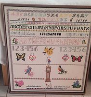Front view of framed counted cross-stitch sampler with alphabets, numbers and decorative motifs