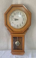 Front view of wooden wall clock showing dial, bezel, pendulum window