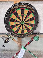 Dufferin bristle dartboard, two fishing rods with attached reels displayed on surface