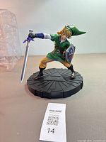 Front view of Link figure on base holding sword and shield; packaging visible