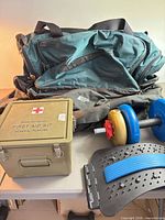 Group shot of both MEC duffels, first aid kit box, dumbbell and back stretcher