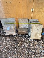 Stacks of square and rectangular stone tiles leaning against plywood wall