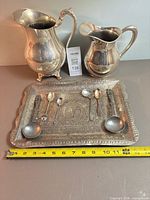 Group shot of tray, two pitchers, four spoons, two ladles with tape measure reference