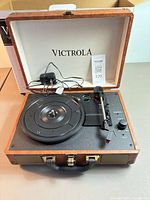 Open Victrola suitcase turntable showing platter, tonearm, control panel and included power adapter