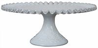 Side view of white milk glass cake pedestal with ruffled clear edge and embossed pattern