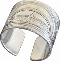 Angled view of open sterling silver band displaying carved orca motif and band opening