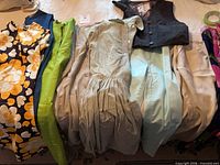 All garments laid out showing variety: floral dress, green pants, beige garments, pinstripe dress, vest, aqua pants