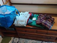 Shirts stacked on dresser with bag visible