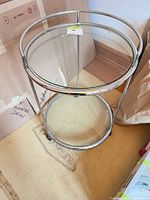 Full view of round chrome bar cart showing both glass shelves and casters