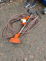 String trimmer with guard and bundled extension cord on paved surface